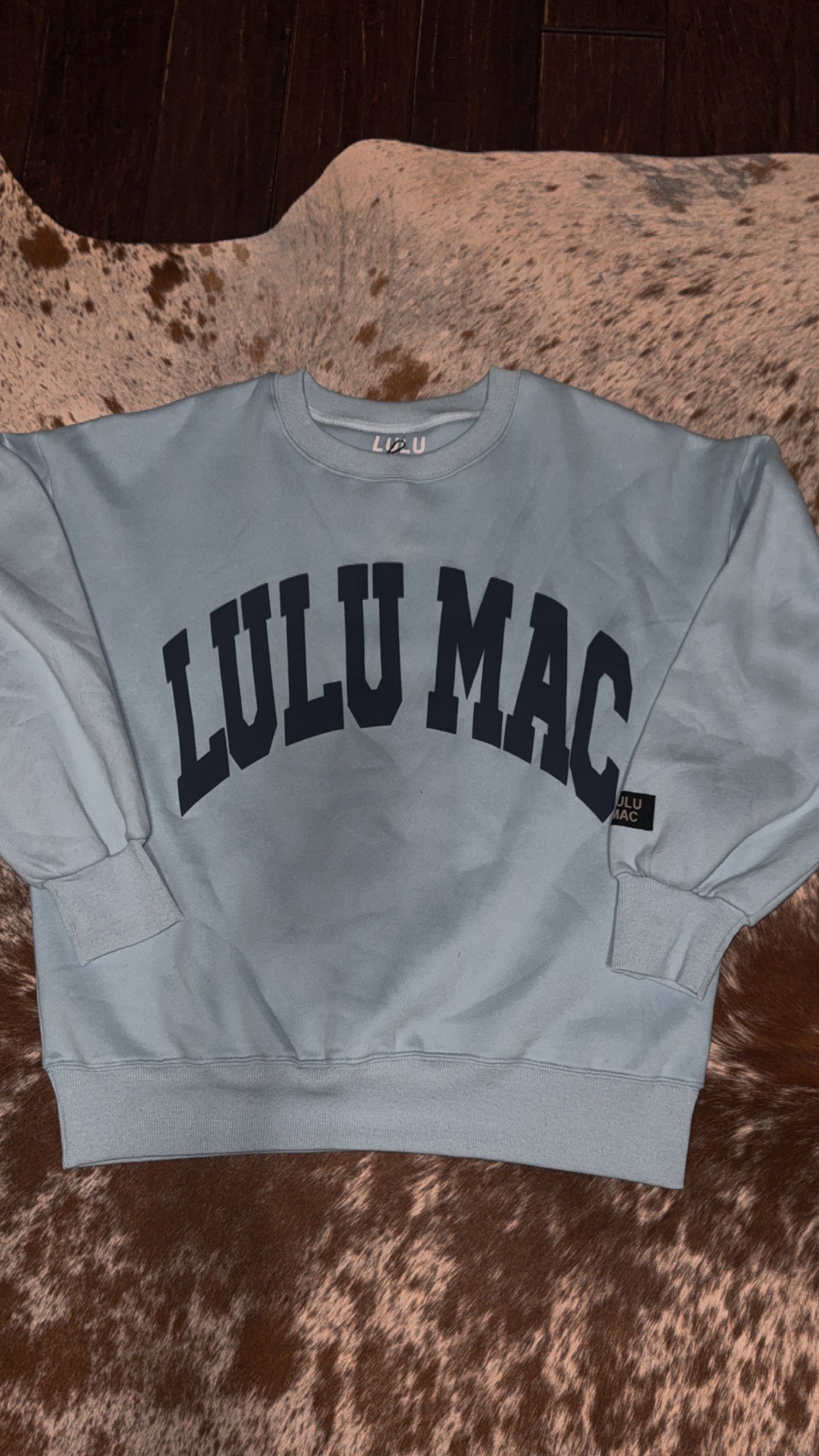 Light blue sweatshirt with 'LULU MAC' text on a textured brown surface
